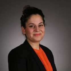 SFSU Professor Ebru Ipek headshot;, woman with dark hair up in a bun, smiling, wearing black blazer and orange blouse